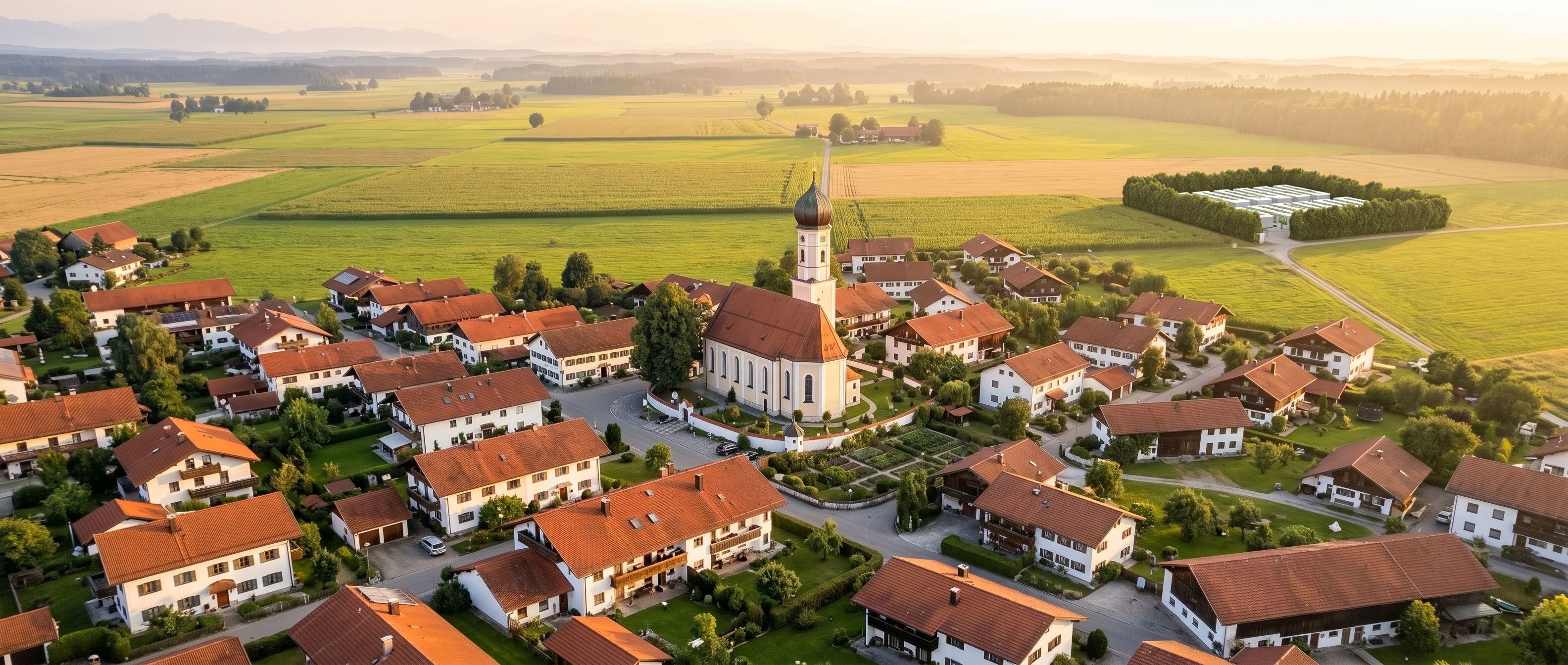 Bayerisches Dorf mit Zwiebelturm-Kirche und dezenter BESS-Anlage am Ortsrand